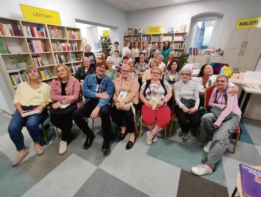 Alek Rogoziński podczas spotkania autorskiego w Filii Bibliotecznej w Racławiczkach, rozmawiający z czytelnikami w wypełnionej sali.