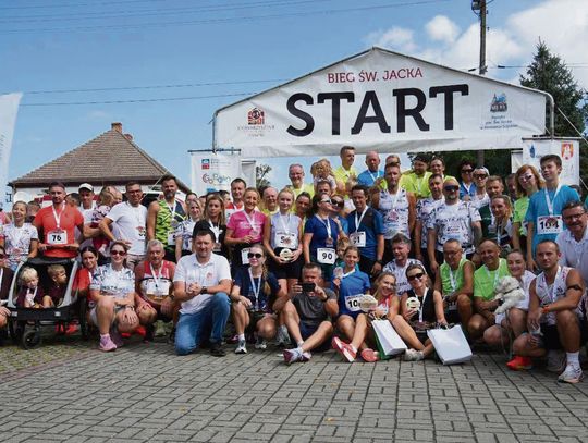 Biegacze na trasie 5,5 km podczas Biegu św. Jacka w Kamieniu Śląskim, w otoczeniu kibiców i zabudowy miejscowości.