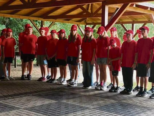 „Młodzieżowe Drużyny Pożarnicze podczas olimpiady obozowej w Dobrej — drużyny w barwach żółtych, zielonych, czerwonych i niebieskich rywalizują na placu ćwiczeń.”