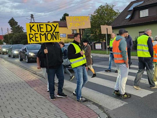 Na zdjęciu mieszkańcy Obrowca stojący przy zniszczonej drodze wojewódzkiej 423, z widocznymi dziurami i ciężarówką przejeżdżającą przez centrum wsi.