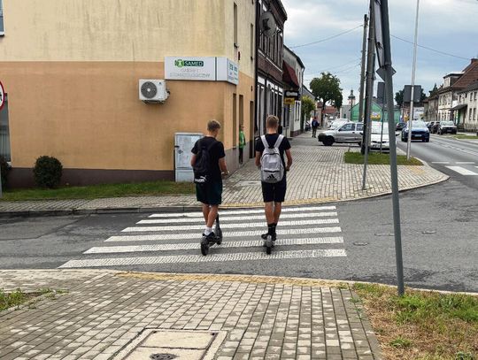 Użytkownik hulajnogi elektrycznej jadący chodnikiem w rejonie zabudowań i sklepów