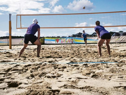 Uczestnicy grający w siatkówkę plażową podczas wydarzenia „Aktywny Orlik” przy ul. Wrzosów, obok stanowisk edukacyjnych dotyczących pierwszej pomocy i zdrowego odżywiania.