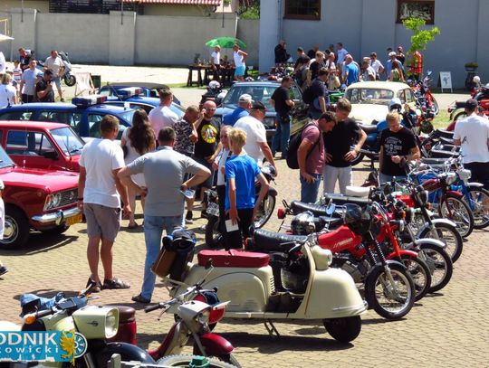 Zabytkowe auta i motocykle zaparkowane na trawie podczas zlotu w Brożcu, z tłumem odwiedzających w tle