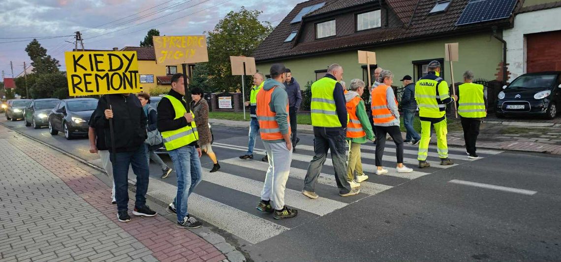 Na zdjęciu mieszkańcy Obrowca stojący przy zniszczonej drodze wojewódzkiej 423, z widocznymi dziurami i ciężarówką przejeżdżającą przez centrum wsi.