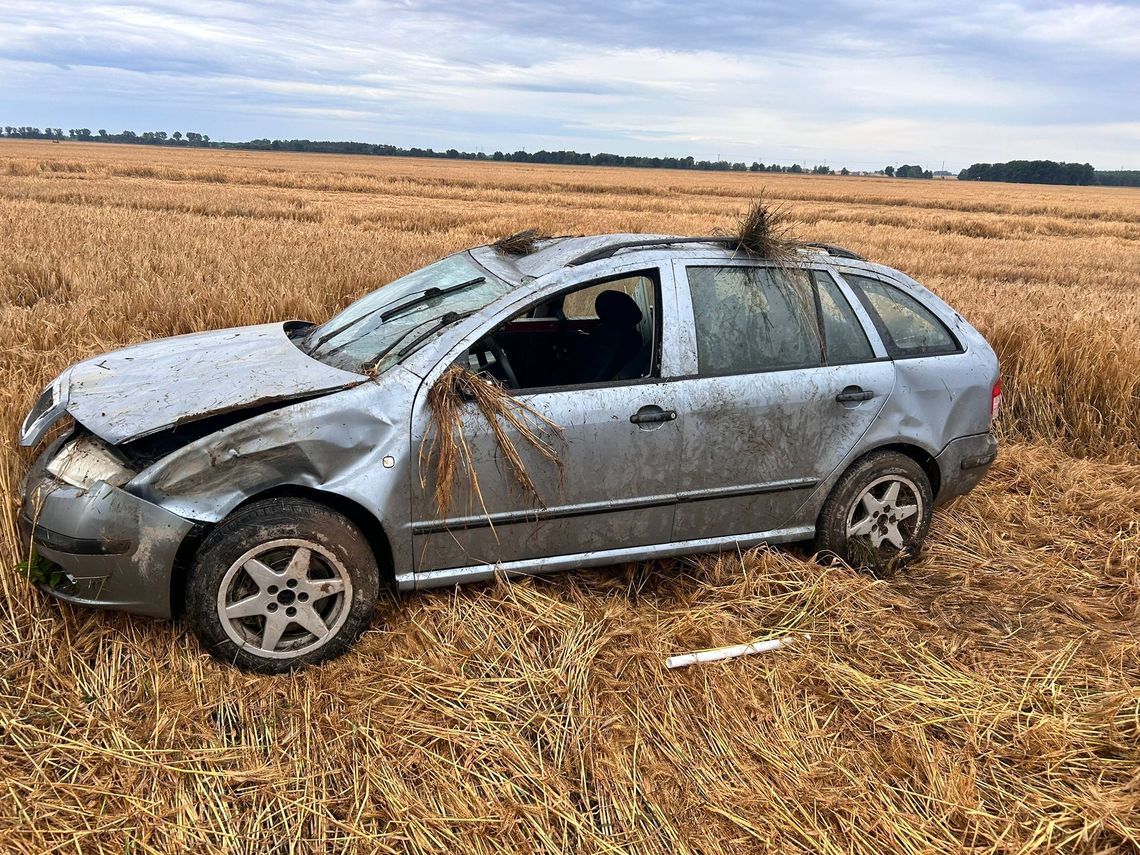Rozbita skoda po dachowaniu w Straduni, stojąca w polu przy drodze krajowej nr 45, w tle strażacy i służby ratunkowe