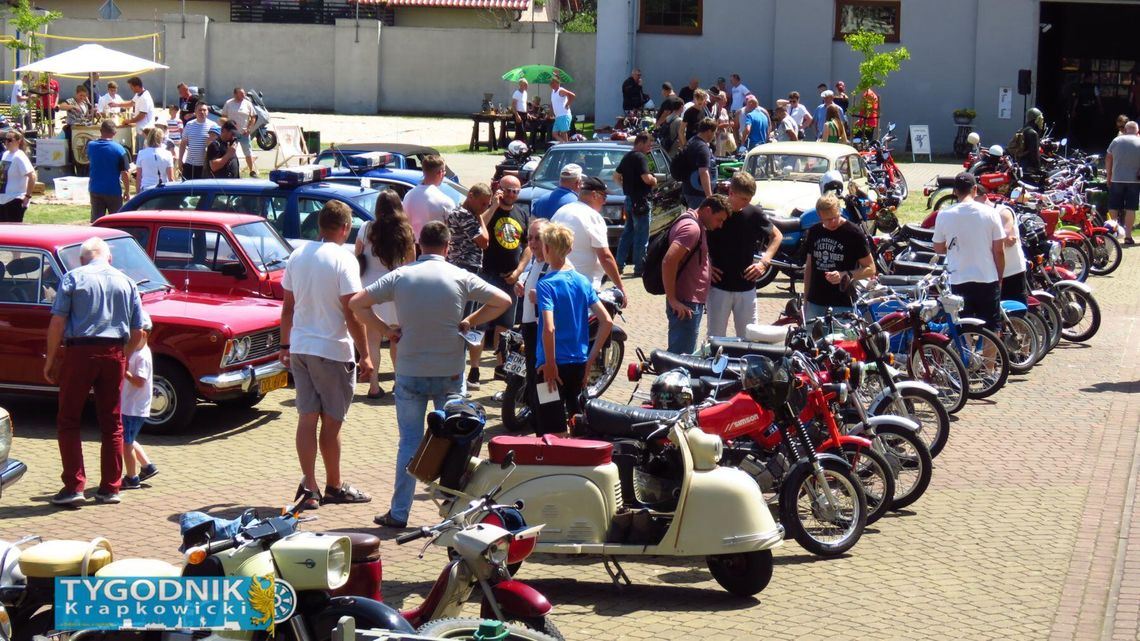 Zabytkowe auta i motocykle zaparkowane na trawie podczas zlotu w Brożcu, z tłumem odwiedzających w tle
